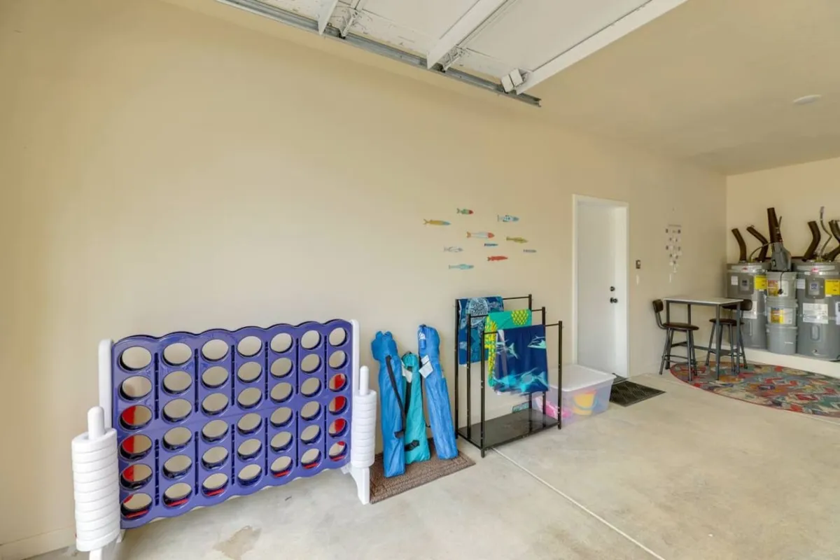 A colorful garage space featuring a large purple connect four game, vibrant fish wall decals, and pool towels, with a storage cart—suggesting a playful, family-friendly environment and ample room for storing outdoor gear and prepping for adventures.