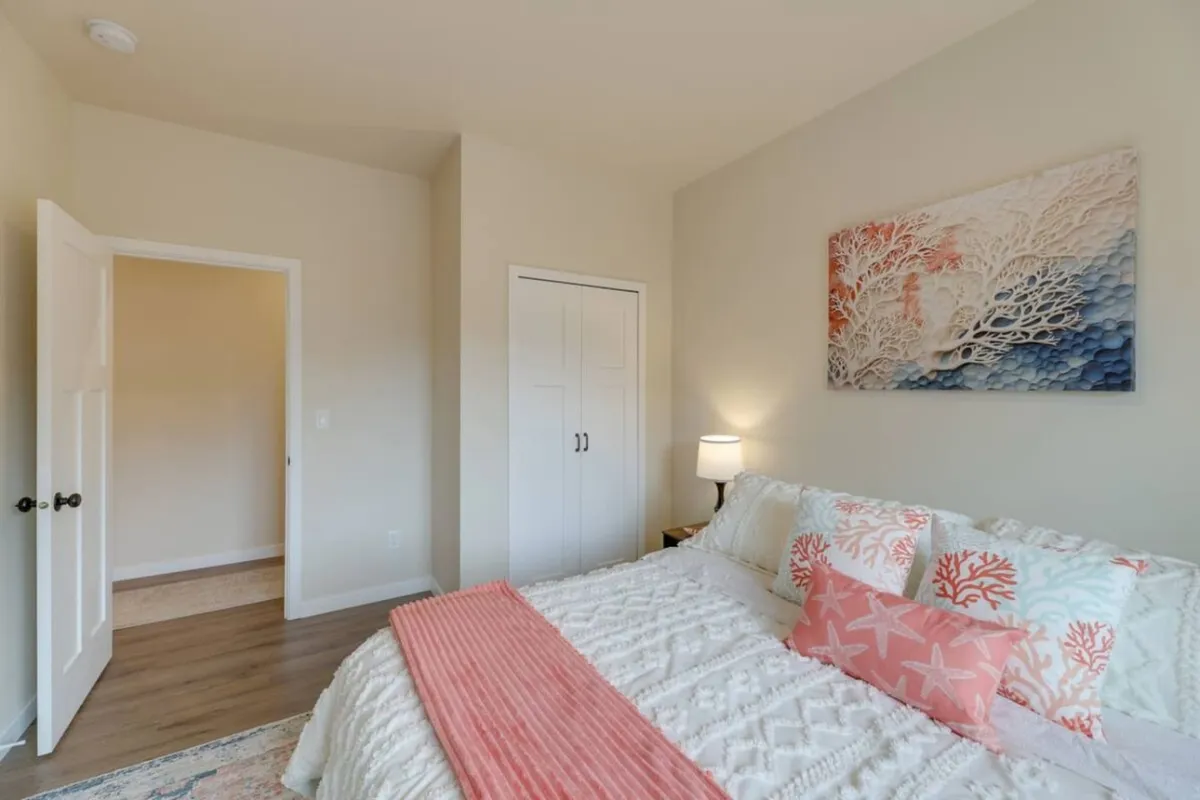 A serene queen bedroom with a bed adorned with decorative pillows, calming wall art, and a softly lit bedside lamp. The large window allows natural light to stream in, creating a cozy and inviting atmosphere perfect for restful nights.