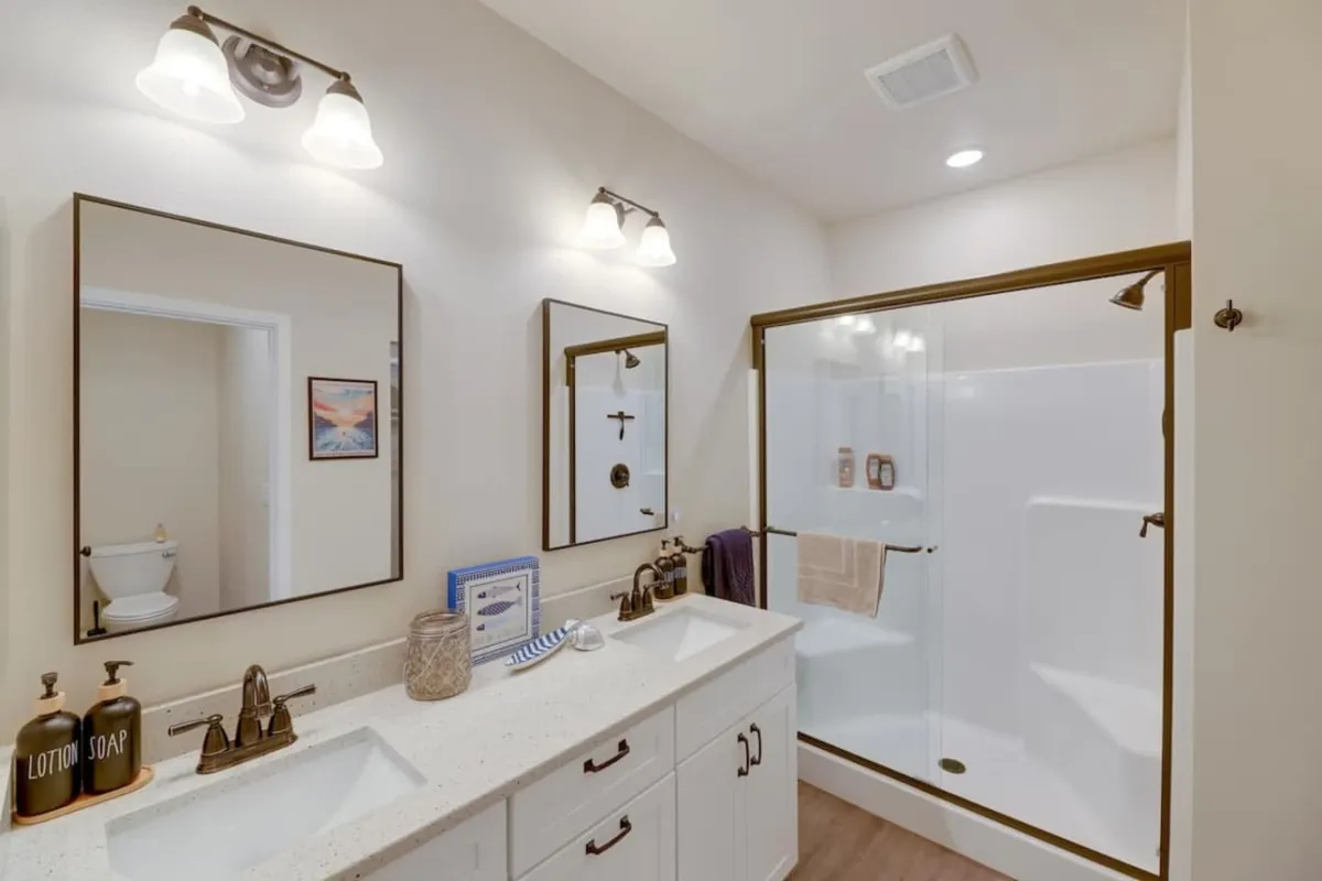 A bright, contemporary bathroom showcasing a double sink vanity, framed mirrors, and a glass shower enclosure. The layout is spacious and practical, ideal for groups needing privacy and ease in their routines.