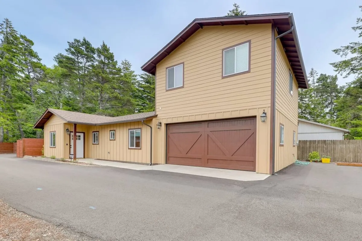 An inviting two-story structure with a wooden garage door and front porch, perfect for gatherings and relaxing outdoors. The spacious yard and welcoming porch set the scene for returning home after a day exploring local gems.