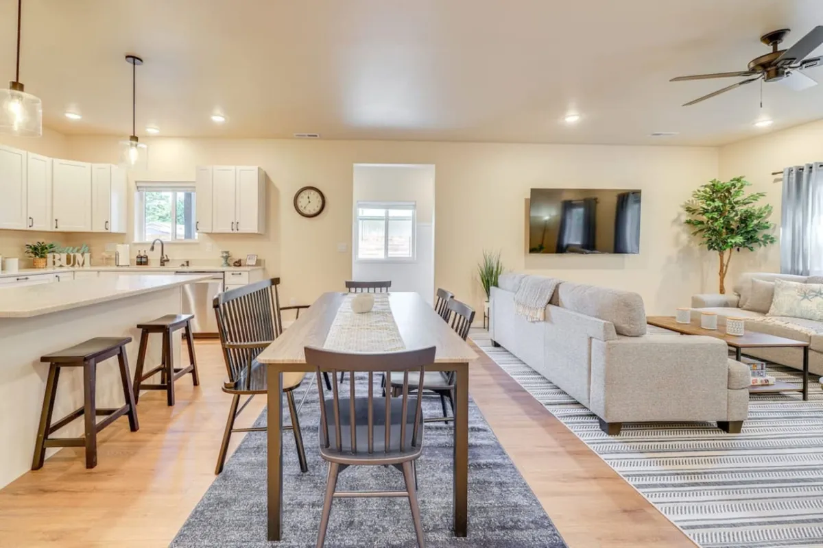 The hero image showcases an inviting open-plan living area with a spacious dining table, comfortable sofa, modern kitchen island, and a large television. There are stylish touches like a potted plant adding warmth, and the space is set up for both relaxing and entertaining, ideal for family gatherings or celebrating special moments.