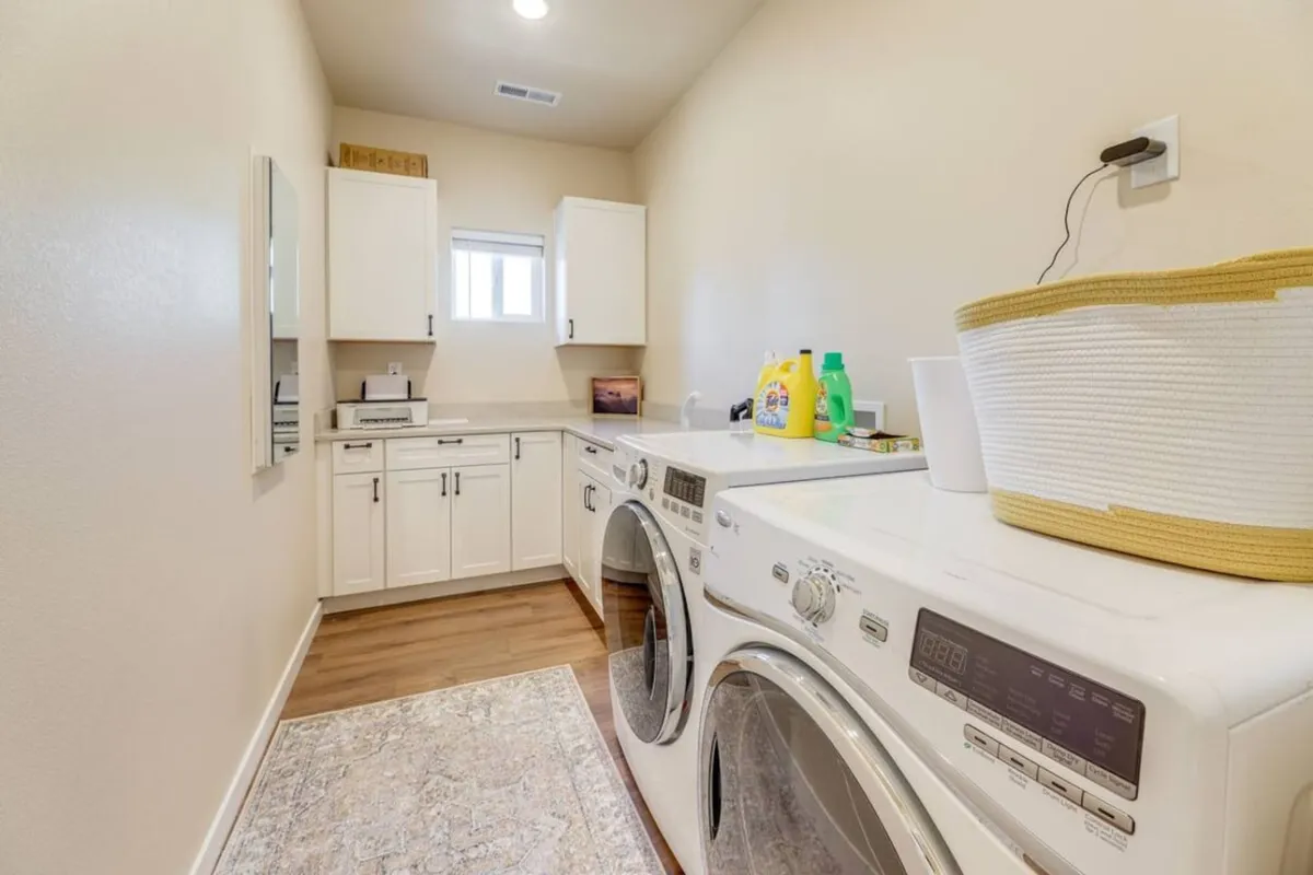 A tidy laundry room featuring a washing machine and dryer, countertop space, a window for natural light, and a laundry basket—suggesting convenience and practicality for guests.