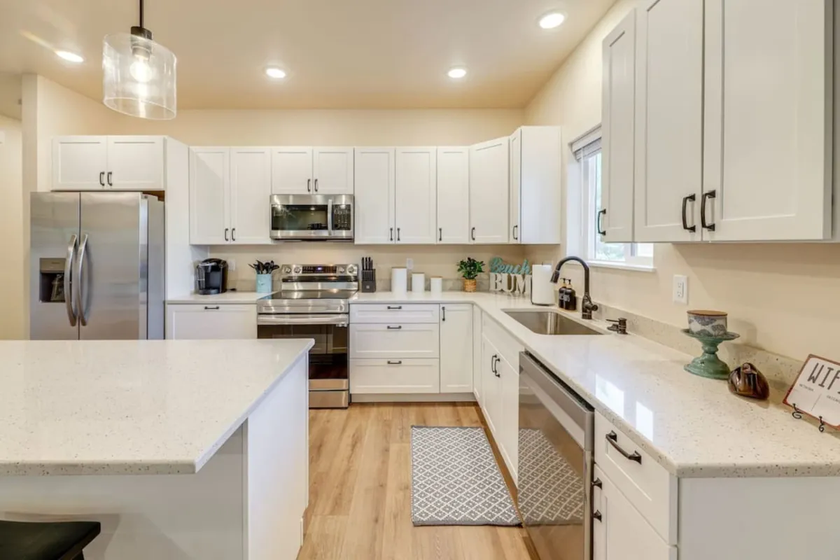 A modern, fully equipped kitchen with a central island, stainless steel appliances, and white cabinetry. The setup is ideal for meal prepping or group cooking, with ample space for interaction.