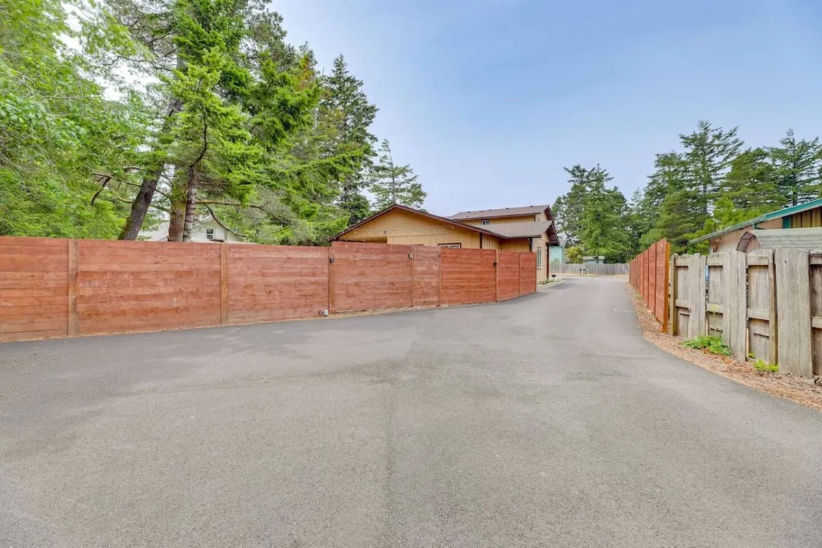 An exterior scene showing a fenced backyard bordered by trees and a paved driveway, offering a sense of privacy and space for outdoor activities.