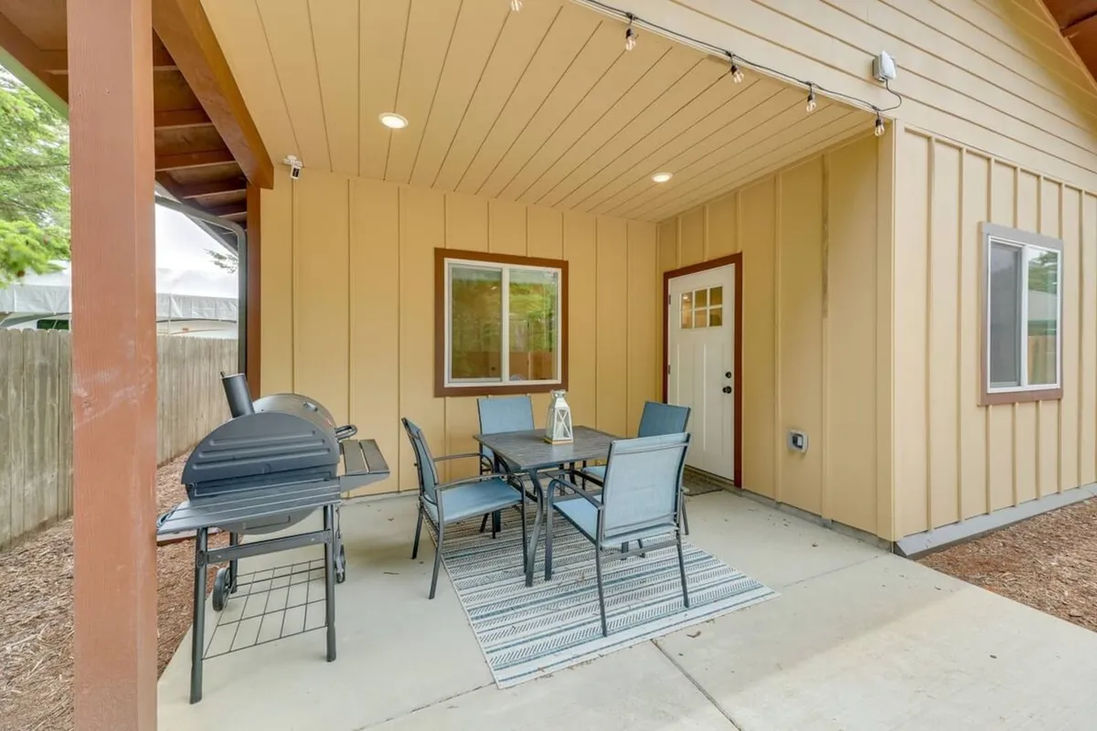 This image features an exterior patio area furnished with a dining table, chairs, a grill, and a rug, just outside a door. String lights suggest the space is usable both day and night, and the setup invites families to relax or dine together outdoors.