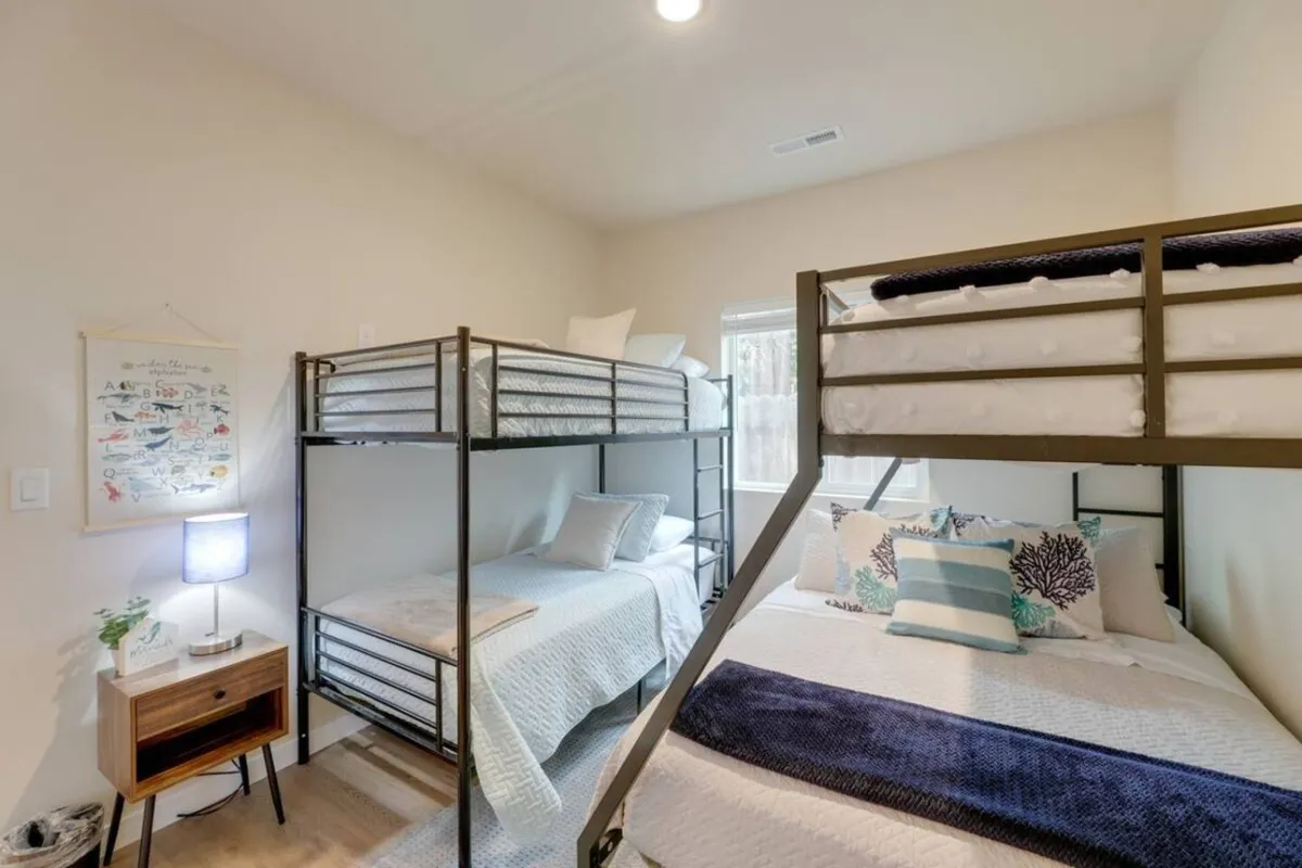 A flexible family bedroom featuring both bunk beds and a large bed with decorative pillows, a nightstand with a lamp, and inviting soft lighting. The arrangement provides ample sleeping options, reflecting the cottage’s ability to accommodate siblings, children, or groups.