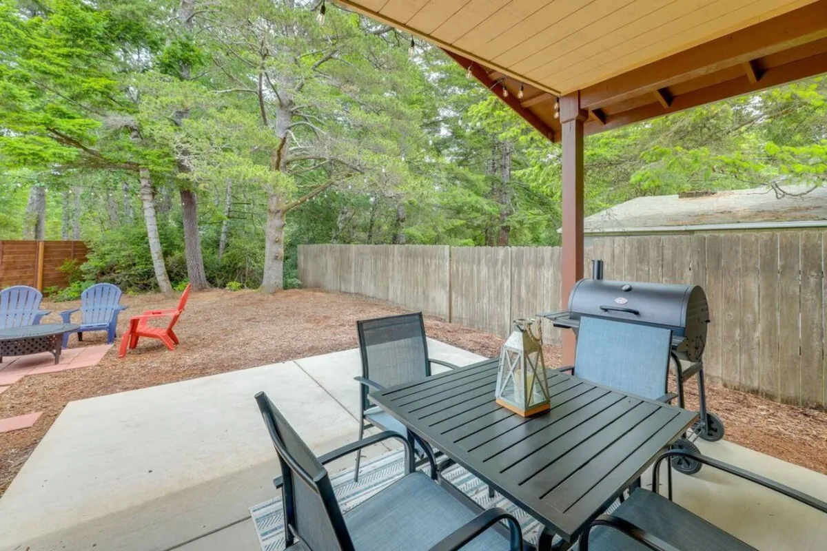 An inviting backyard scene featuring an outdoor dining table set up for meals, a grill for barbecuing, Adirondack chairs for lounging, and a fenced grassy area—sunset lighting and open sky enhance the sense of relaxed coastal living.